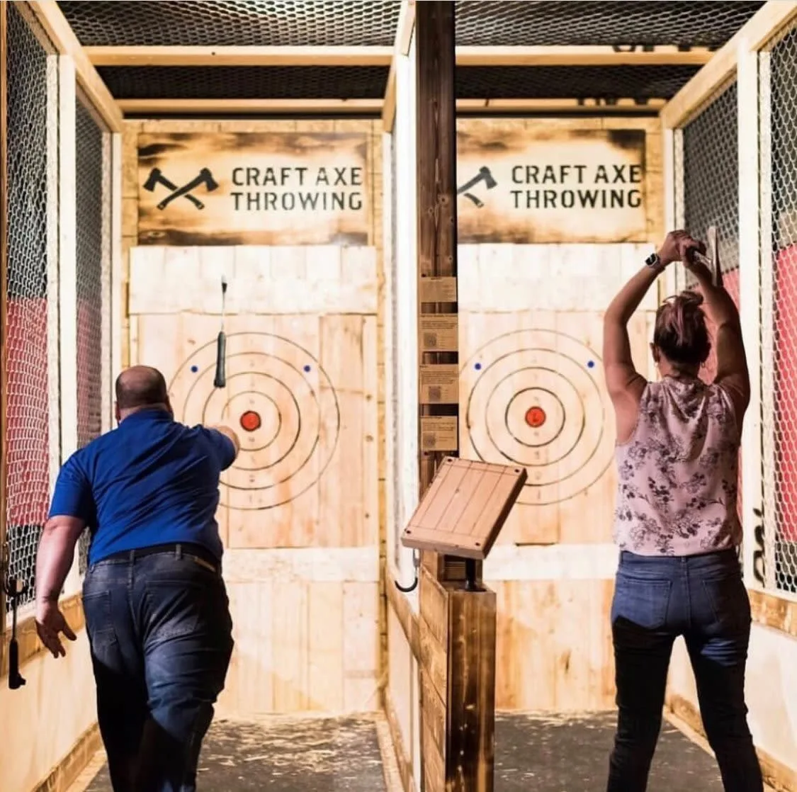 Two throwers on side-by-side axe throwing lanes with bullseye targets