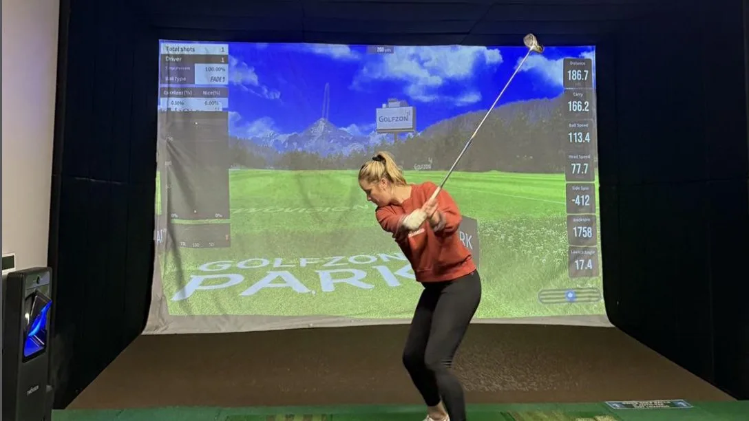Golfer swinging in a Golfzon simulator bay at 9Yards Golf Lounge, with shot data on the screen