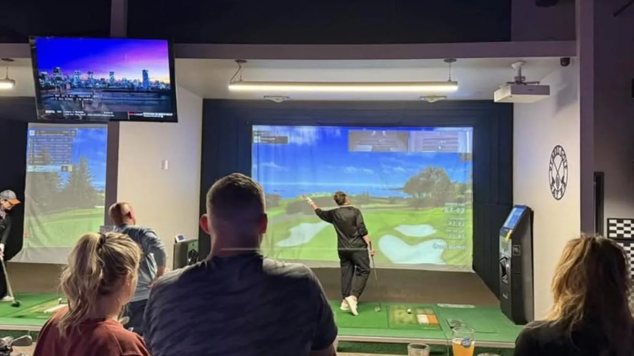 Guests at the bar watching a golfer play a simulator bay at 9Yards Golf Lounge, with more bays in the background
