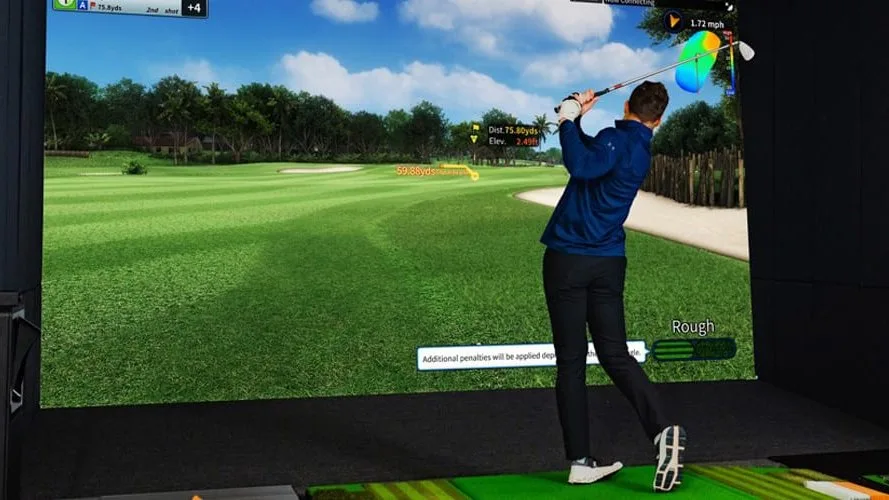 Golfer finishing a swing in a simulator bay while ball flight data shows on the screen