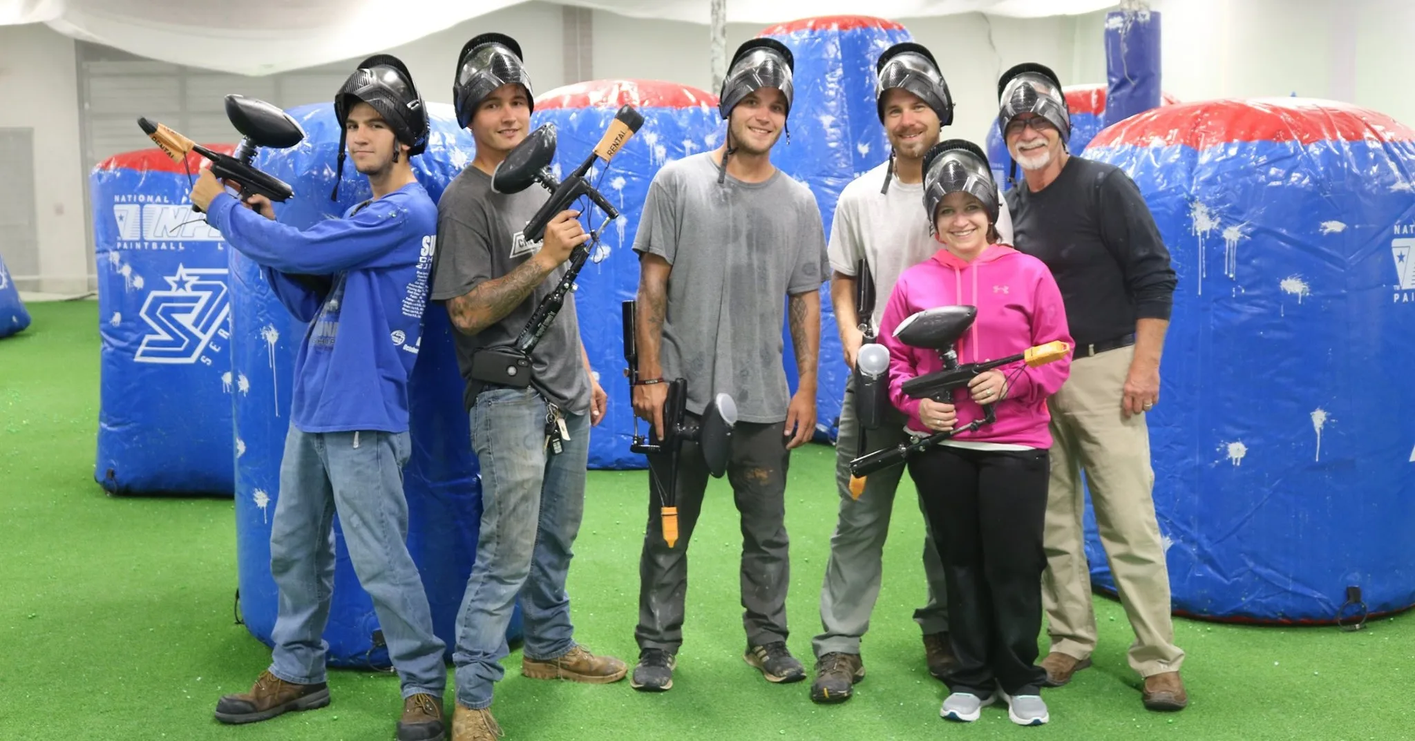 Group of players in masks with rental markers inside an indoor paintball arena